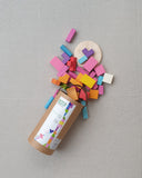 Colorful wooden puzzle pieces spilling out of a cardboard box on a gray surface