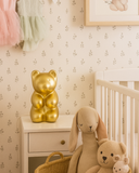 Children's room with toys, a gold bear lamp, and framed artwork on floral wallpaper.